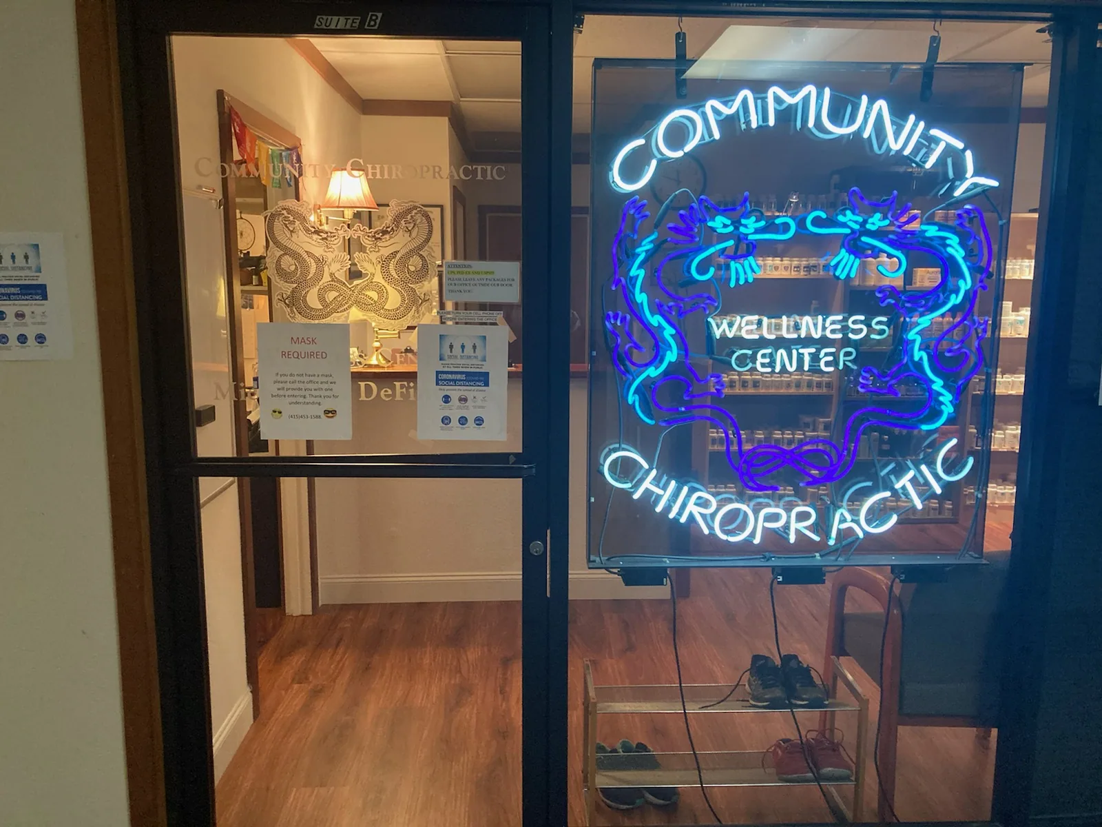 Community Wellness Center Chiropractic neon sign in storefront window with blue door frame and wooden interior visible
